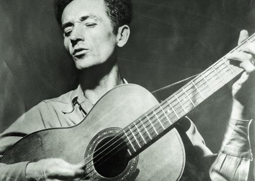 WOody Guthrie holding an acoustic guitar 